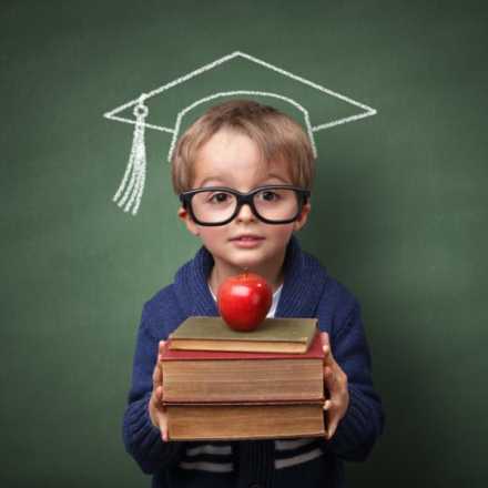 Kid with books and apple in front of chalk board with graduation hat drawn on it.