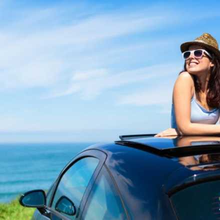 woman popping out of sunroof in car in front of the ocean