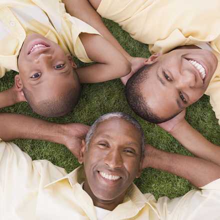 Father and two sons laying on grass looking at camera smiling