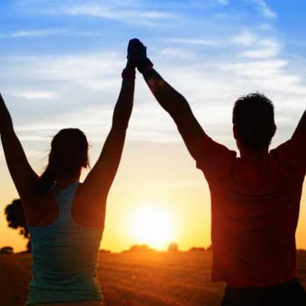 man and woman arms raised holding hands at sunset
