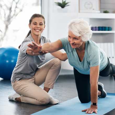 older women on yoga mat training her balance with a young trainer