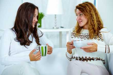 Two women sitting on a couch drinking coffee
