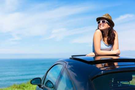 woman popping out of sunroof in car in front of the ocean