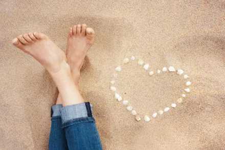 Bare feet in the sand with seashells making a heart shape