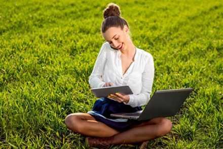 woman sitting on grass with laptop and ipad