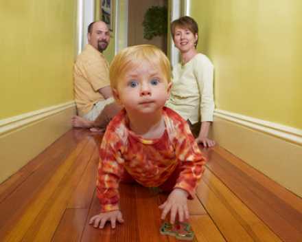 baby crawling on wood floors in hallway, parents in background smiling