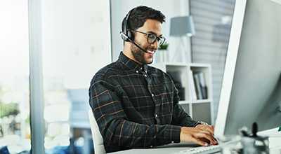 Man happily typing on keyboard and talking on headset