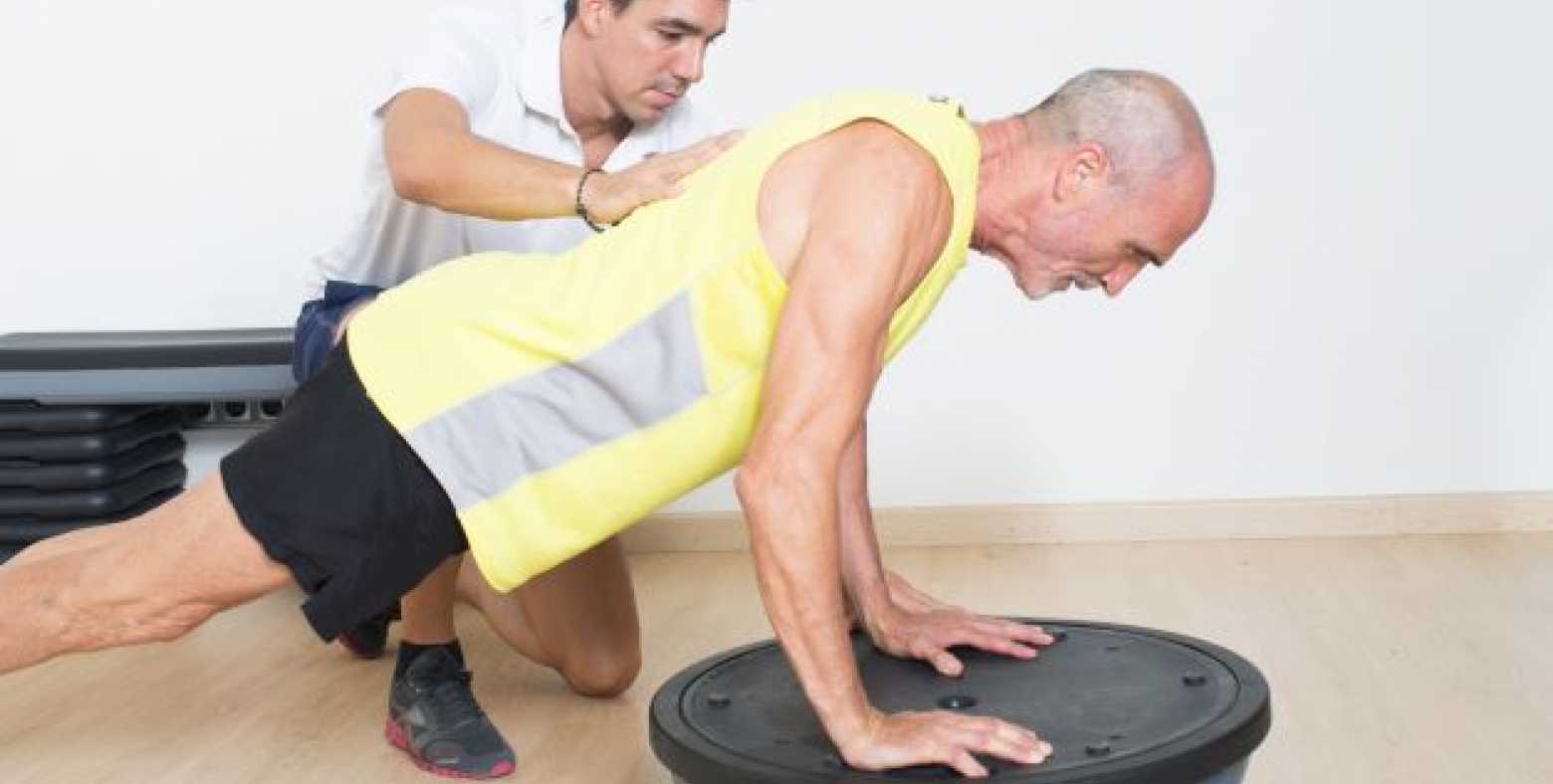 senior planking on bosu ball with personal trainer on side
