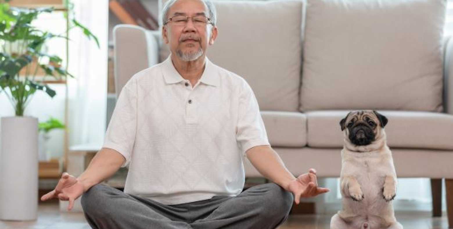 senior male in meditation pose with dog beside him
