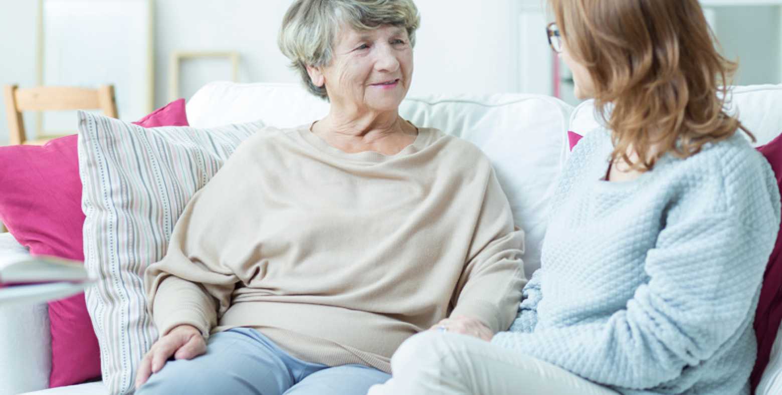 elderly woman and middle-aged woman sitting on couch talking