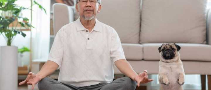 senior male in meditation pose with dog beside him