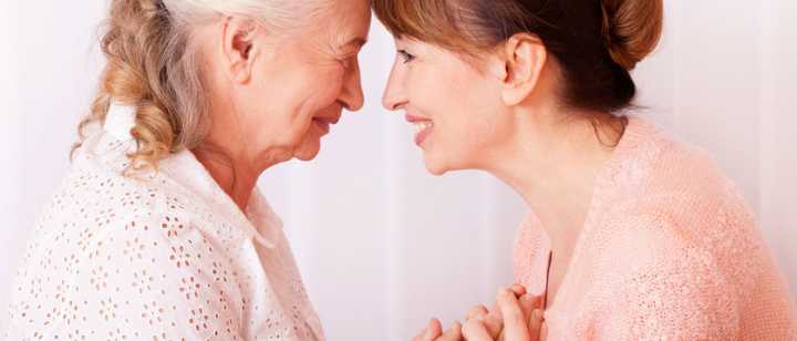 elderly mother and daughter holding hands, smiling face-to-face with foreheads touching