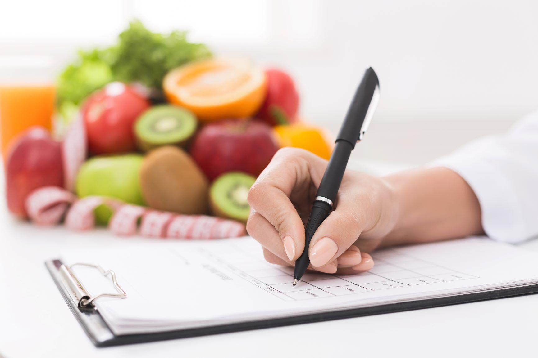 nutrition professional writing notes on clipboard with fruits in background
