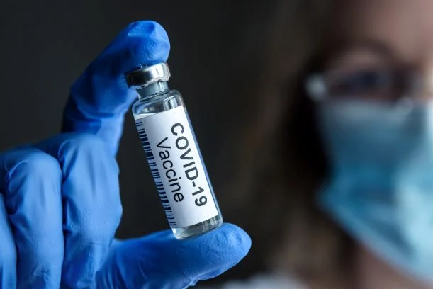 gloved hand holds vial with inscription: COVID-19 vaccine