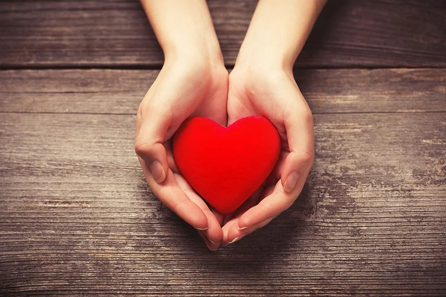 hands gently cupping a red heart