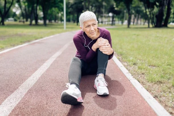 senior-woman-knee-1283901451_Small woman sitting on track field holding her knee