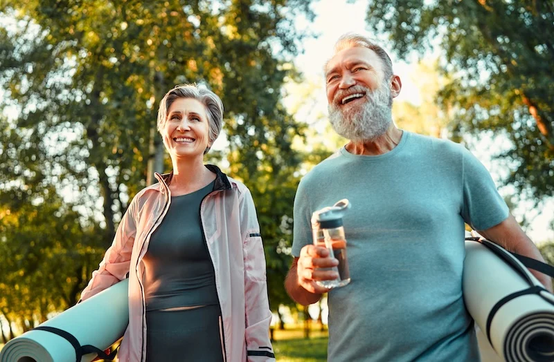 middle-aged couple walking outdoors with yoga mats
