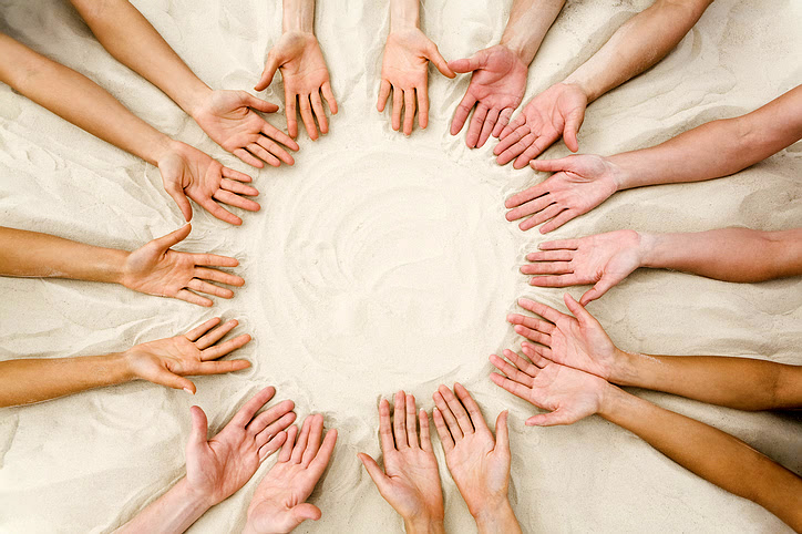 Image of several friendsv hands on sand in the form of circle hands in a circle with open palms