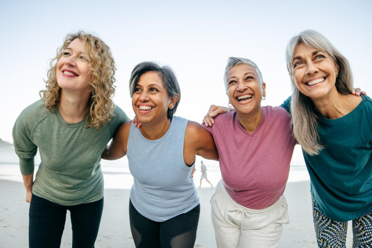 4 joyful women stand with arms wrapped around each other's backs