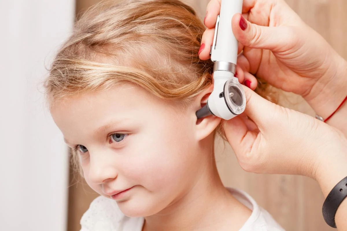 pedent doctor checks child's ear with instrument