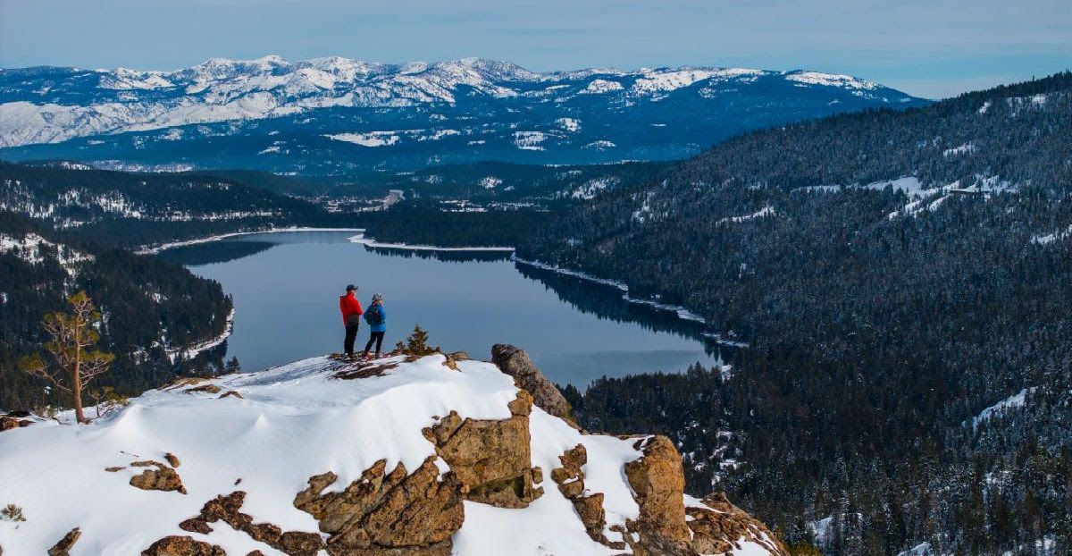 wide view of two people standing on a summit overlooking donner lake