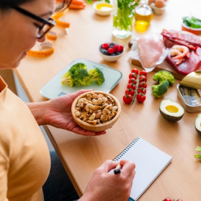 woman writes in food diary as she hold a bowl of nuts