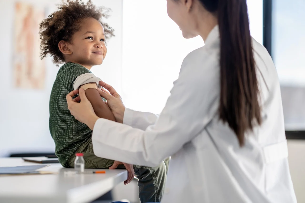 Young boy receives bandaid on upper arm after receiving vaccine