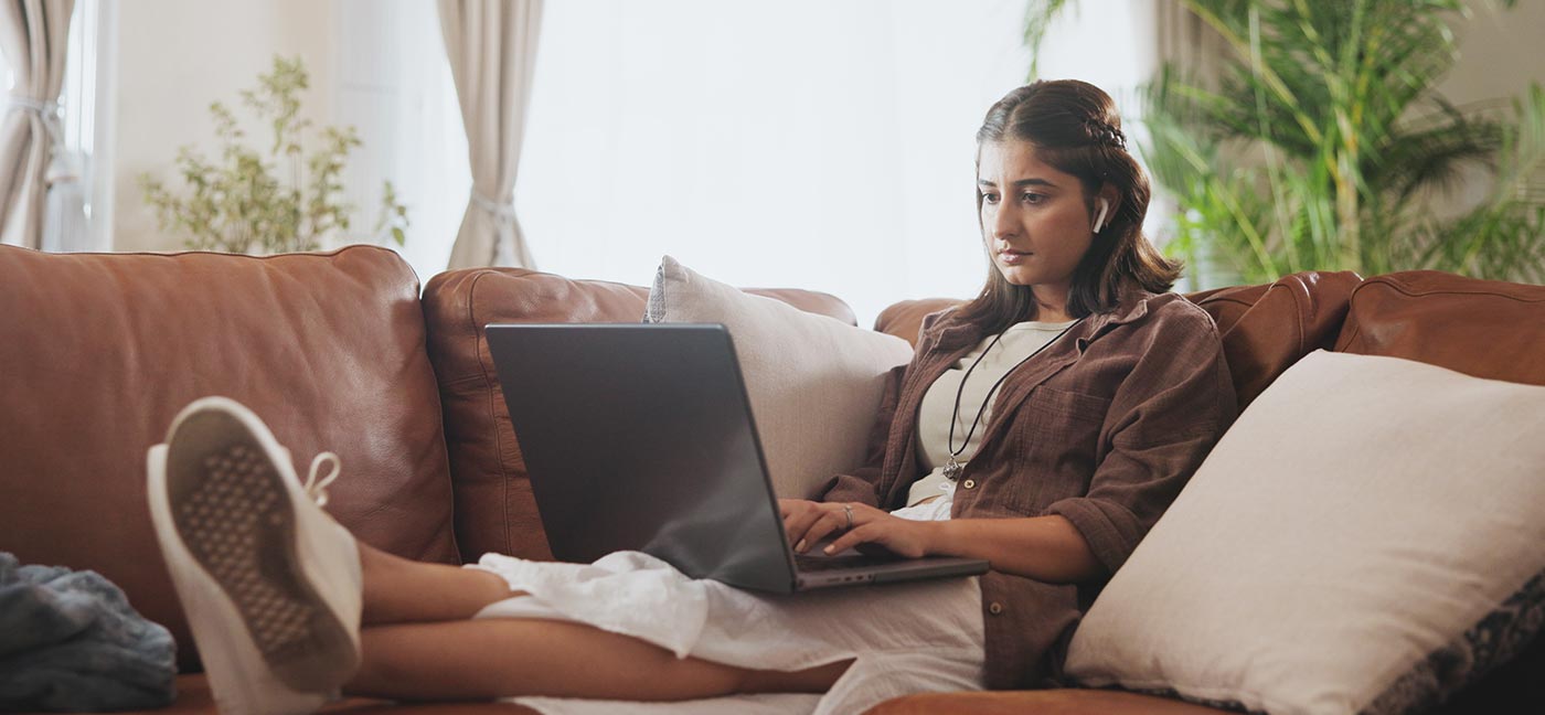 Woman on a couch using a laptop with her feet up