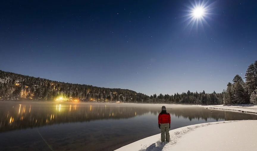 Donner Lake with snowshoer looking up at bright moon