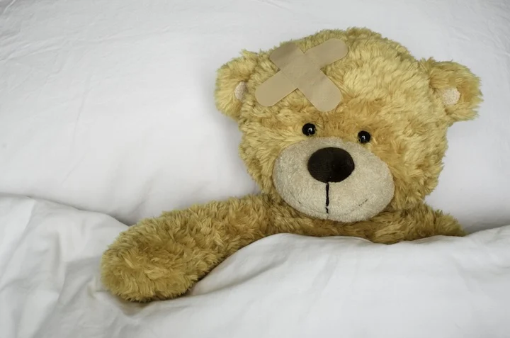 teddy bear with bandage on its head in bed
