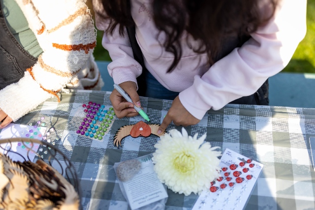 Child decorating a wooden heart with wings at a picnic table