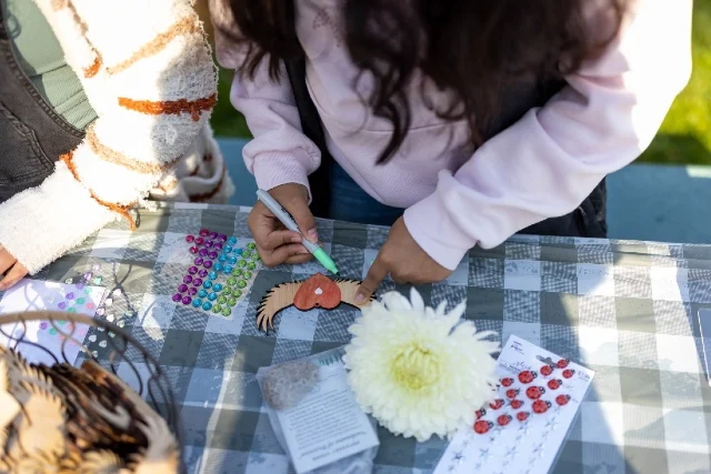 Child decorating a wooden heart with wings at a picnic table