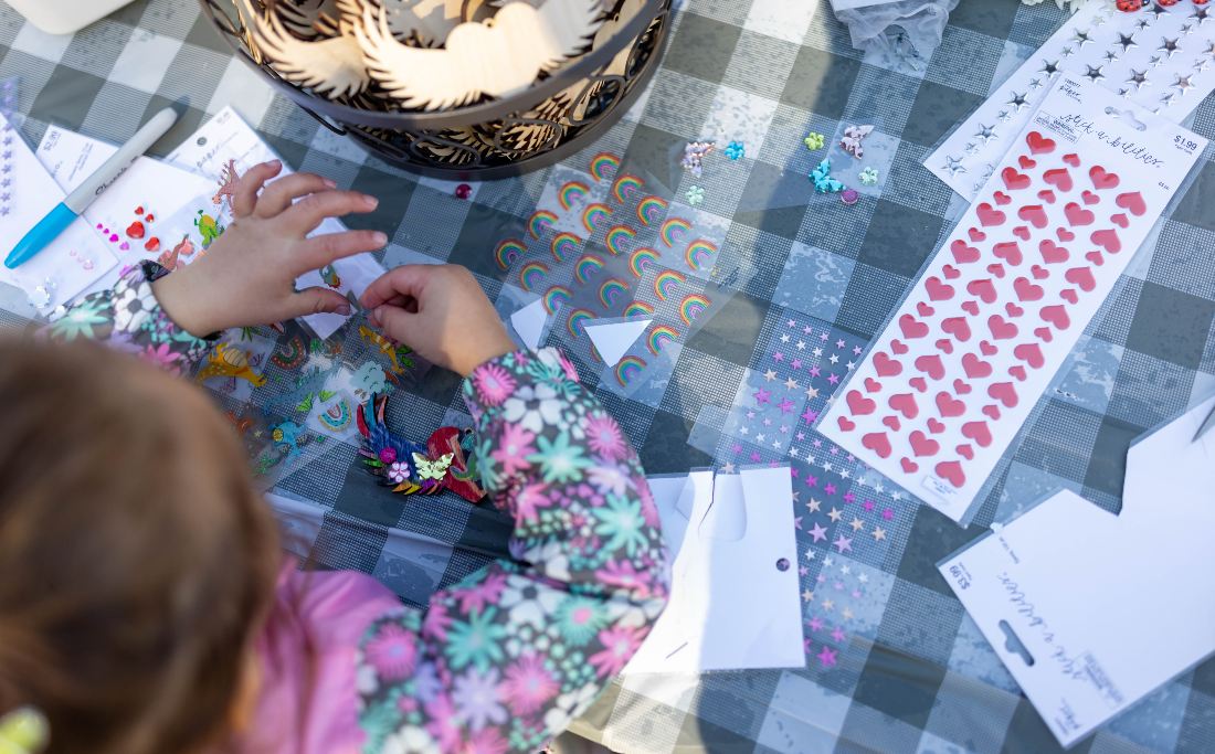 Child's hands decorating a card with stickers at a picnic table