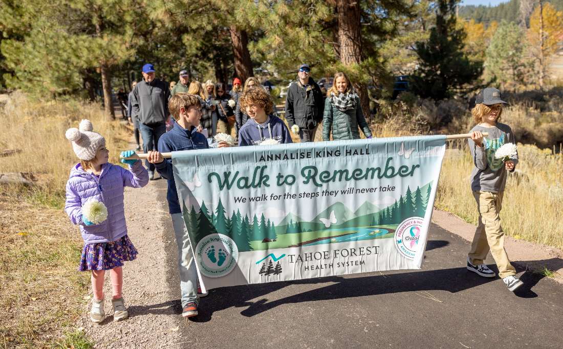 Group of walkers, including children, carrying the Walk to Remember banner along a wooded trail