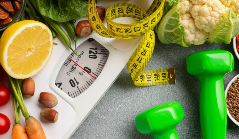 weightloss scale, measuring tape and weights arranged with vegetables