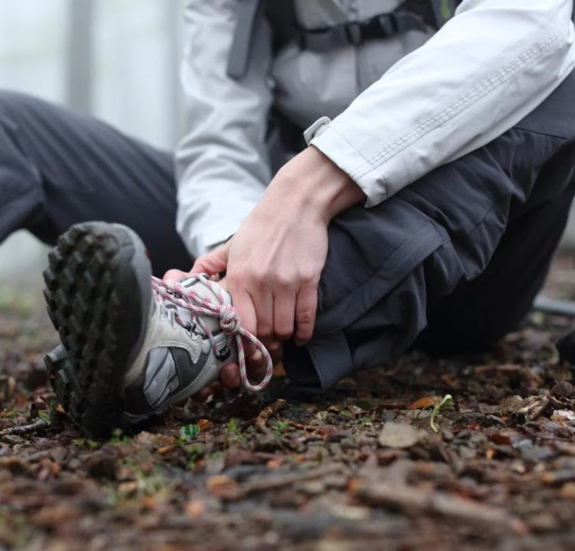 person holds ankle while sitting on the ground