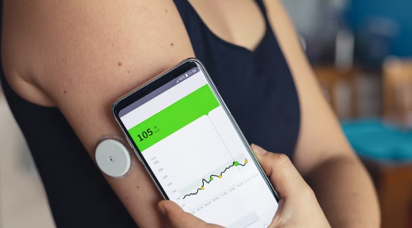 woman holds phone to continuous glucose monitor on back of arm