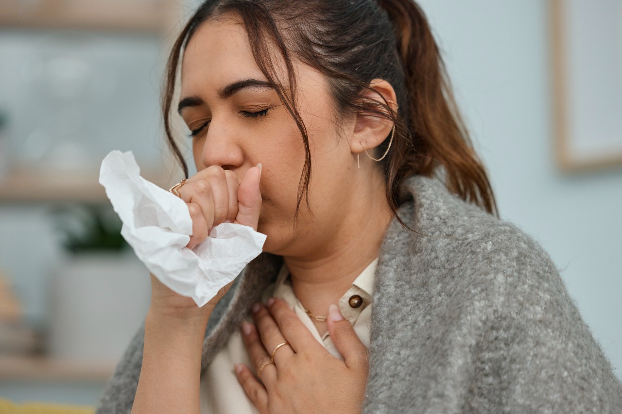 woman coughs into napkin in hand and holds chest